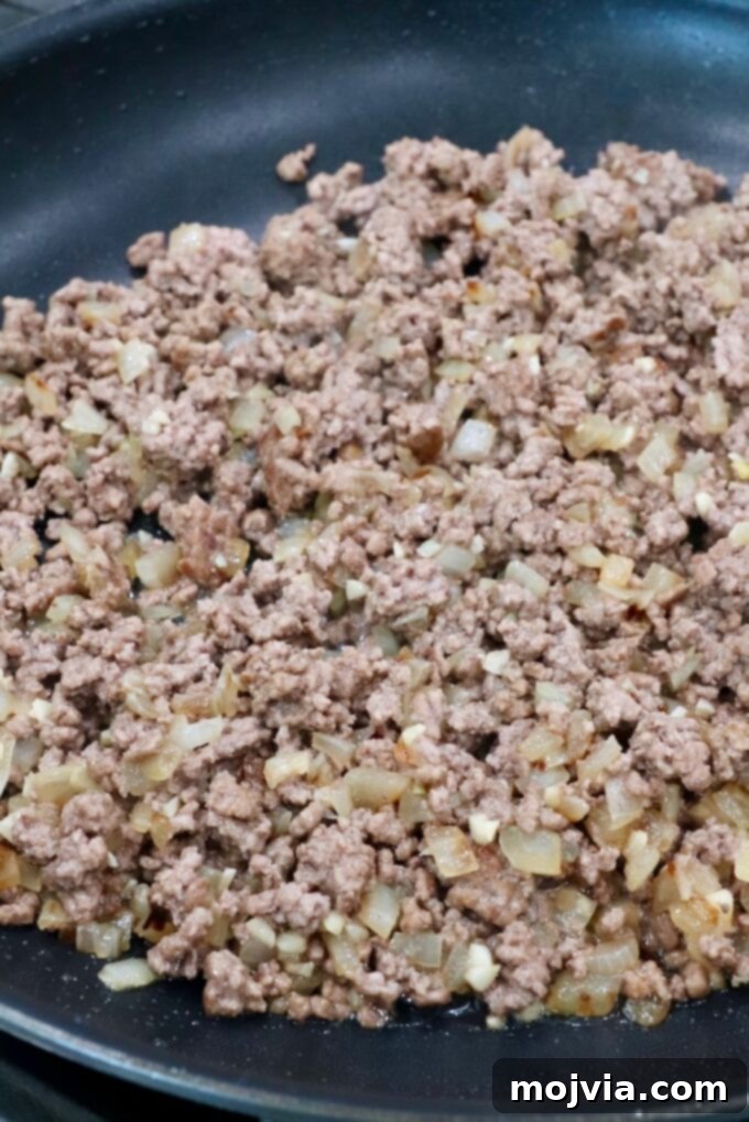 Robust Chili Burger 5 Cooked and browned ground beef with softened diced onions in a skillet, after draining grease.