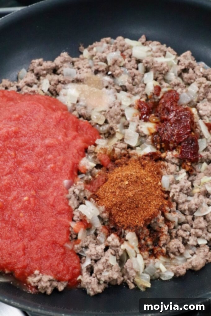 Robust Chili Burger 6 Seasoned ground beef with a can of crushed tomatoes added to a skillet for chili preparation.