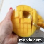 mango sliced into cubes in the skin with a spoon in the mango
