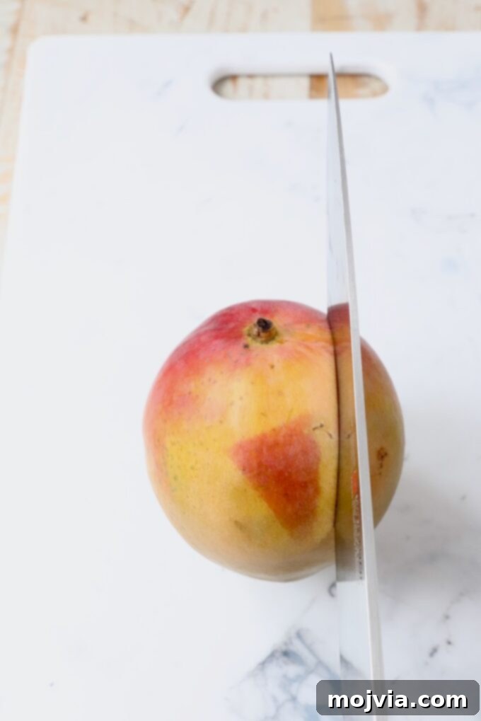 The Art of Mango Slicing 3 Sharp knife making the first cut along the side of a mango, demonstrating proper positioning away from the pit