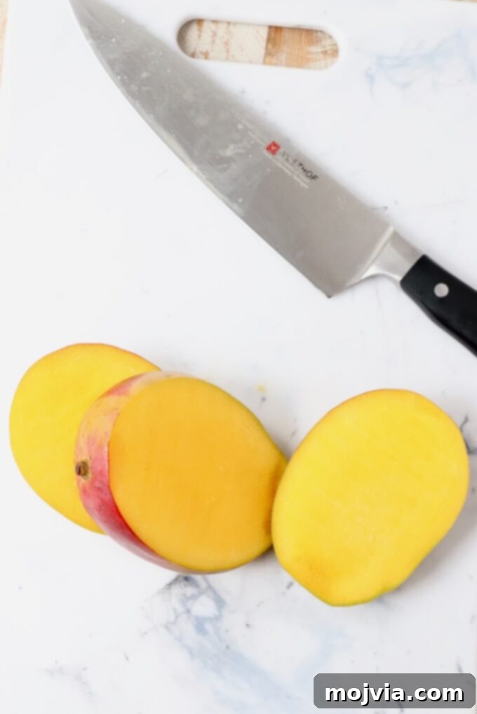 The Art of Mango Slicing 4 Two large mango cheeks separated from the central pit, resting on a cutting board beside a knife