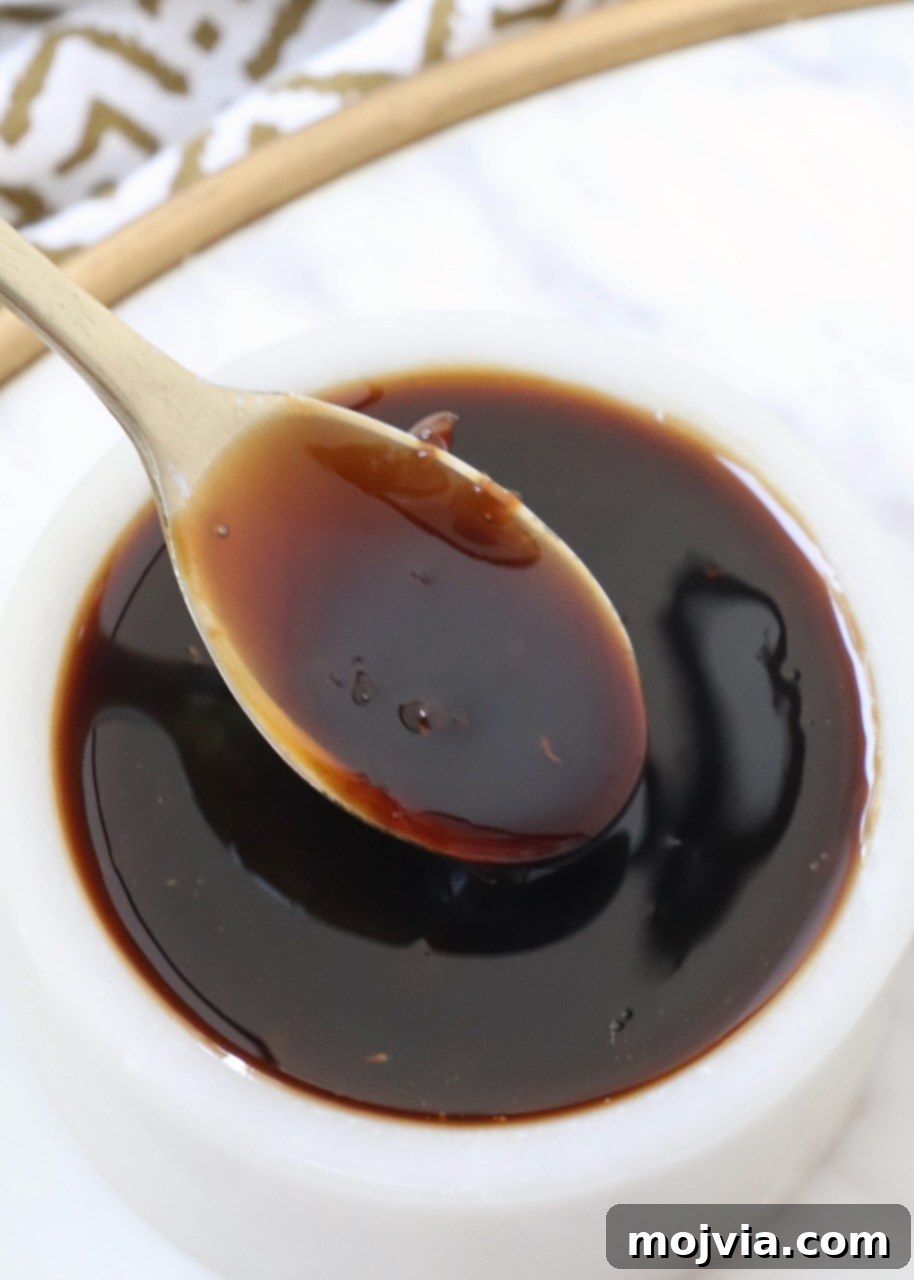 Umami Glaze 2 A small bowl filled with rich, glossy homemade teriyaki sauce, accompanied by a tiny serving spoon, ready for use.