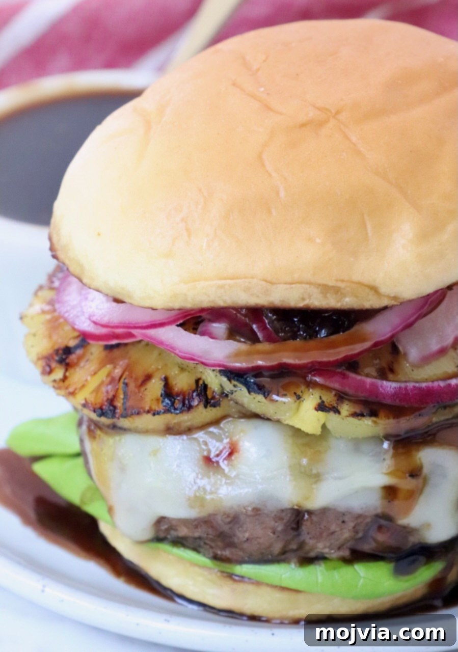 Umami Glaze 6 A delicious cheeseburger topped with a slice of grilled pineapple and vibrant pickled onions, served on a plate and ready to eat.