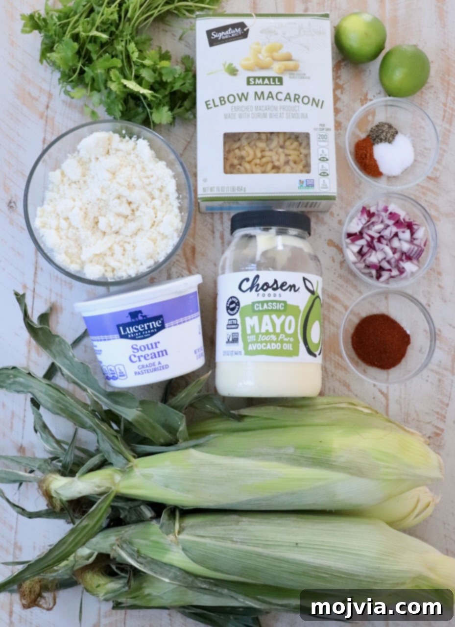 Ingredients for Mexican street corn pasta salad laid out on a white wooden board, including corn, pasta, red onion, cilantro, cotija cheese, sour cream, mayonnaise, and spices.