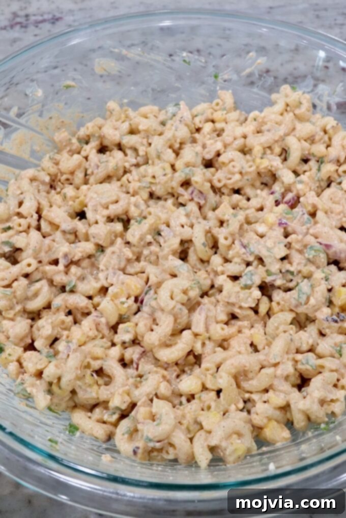 The Mexican street corn pasta salad fully assembled in a large glass bowl, ready for chilling and serving.