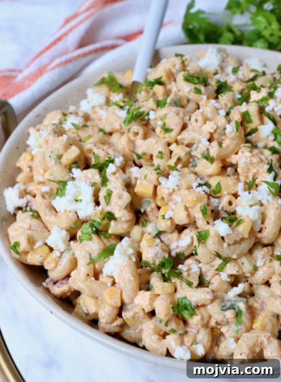 Mexican street corn pasta salad in a bowl with a serving spoon, ready to be enjoyed.