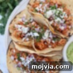 tacos on plate filled with cooked, shredded chicken, cheese, diced onions and cilantro