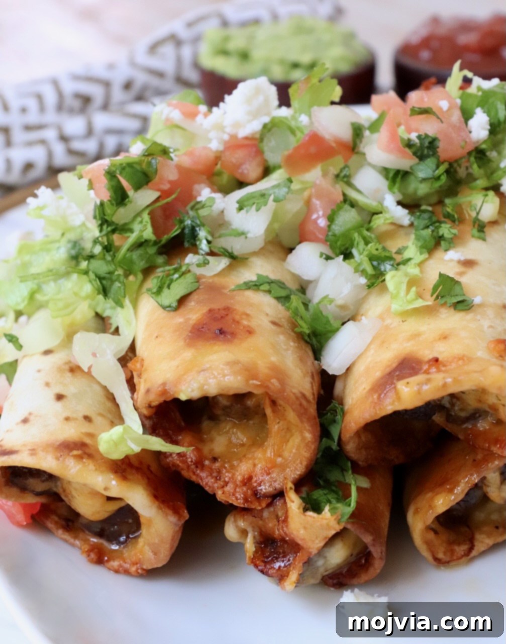 Crispy Beef Taquitos 2 beef taquitos stacked up on plate topped with pico de gallo