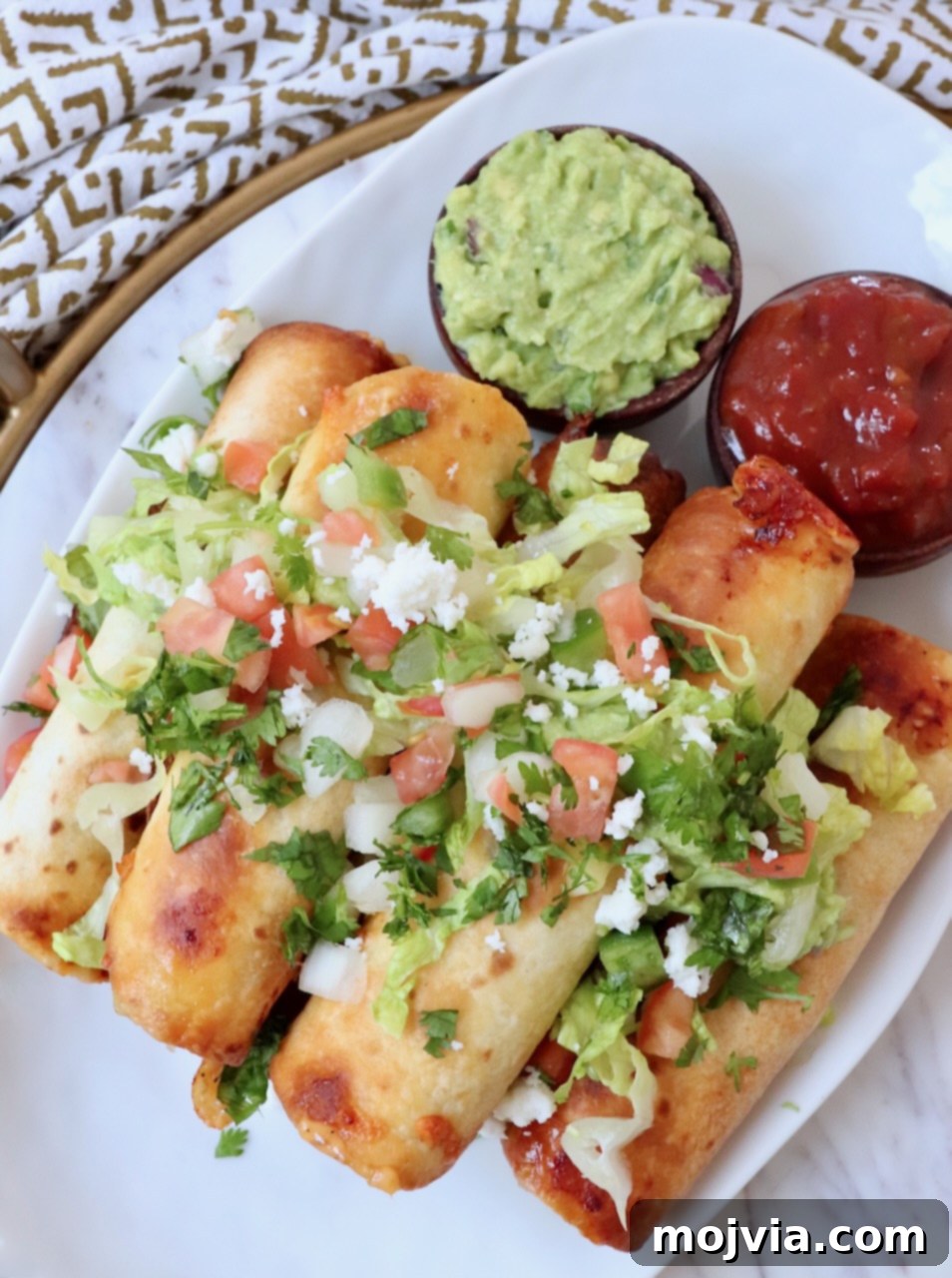 Crispy Beef Taquitos 11 taquitos stacked up on plate topped with guacamole and pico de gallo