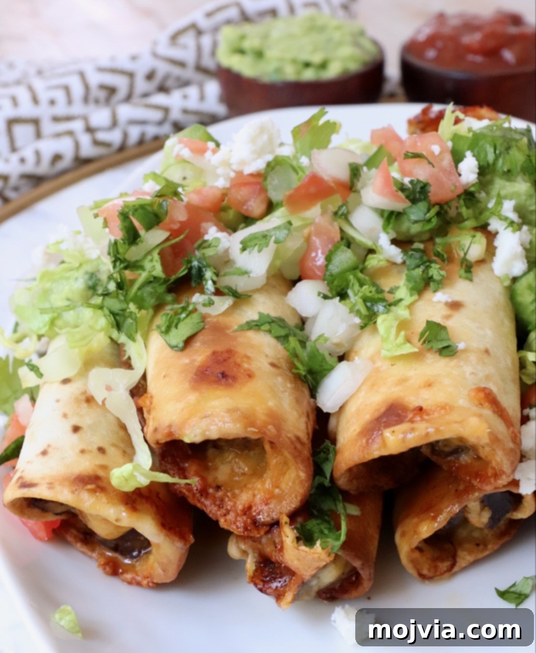 Crispy Beef Taquitos 12 cooked beef taquitos stacked up on a plate topped with pico de gallo