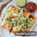 taquitos stacked up on plate topped with guacamole, pico de gallo and cilantro