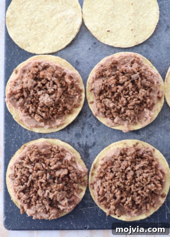 tostada shells topped with refried beans and ground beef on a cutting board