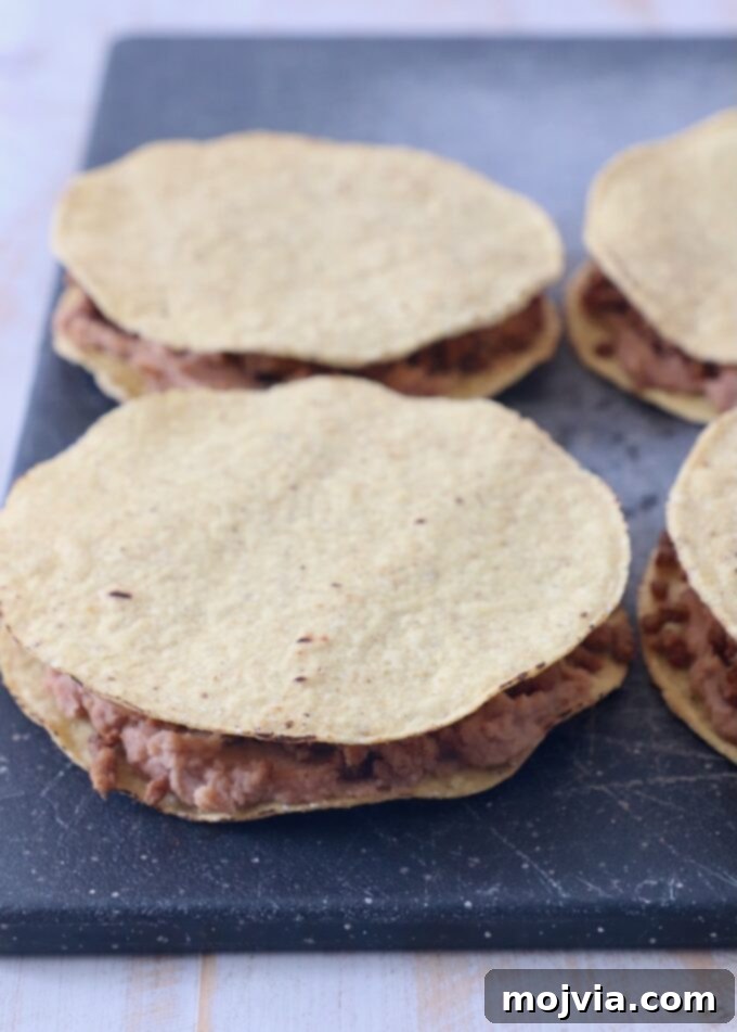 ground beef and refried beans sandwiched between tostada shells on a cutting board