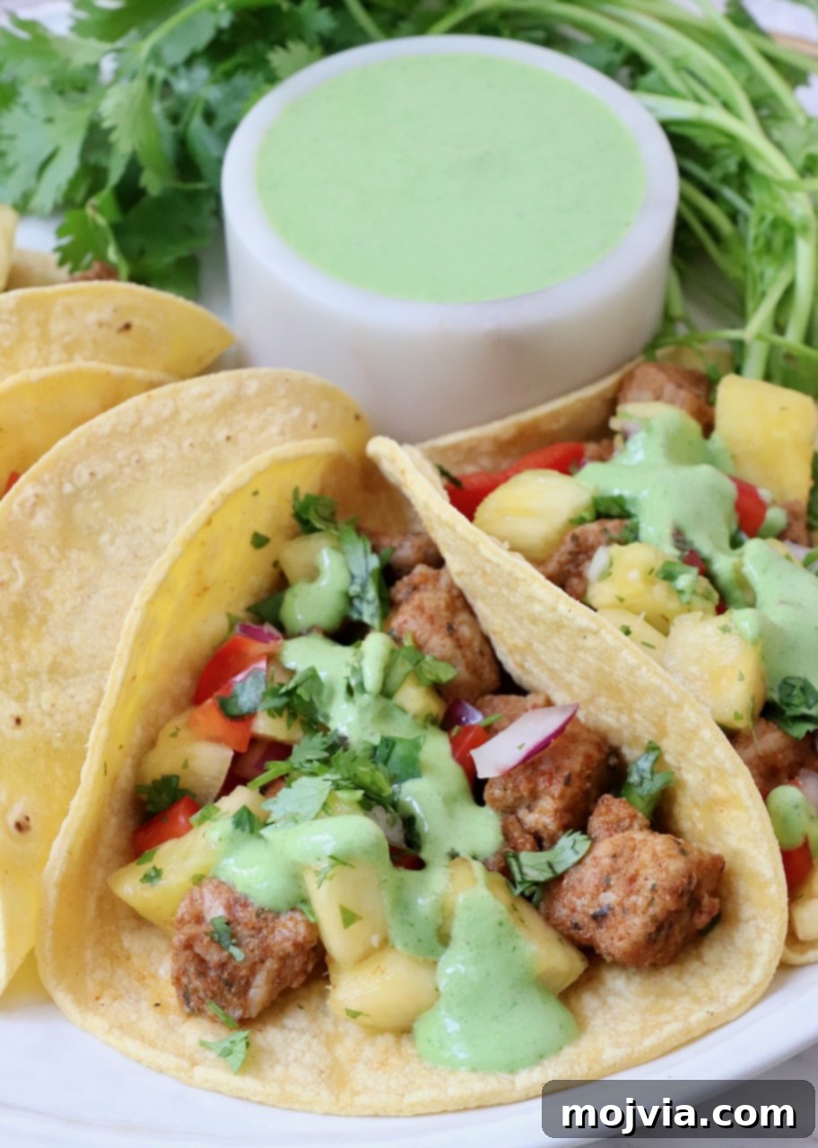 Zesty Carnitas Tacos 6 A close-up shot of pork tacos drizzled with cilantro lime sauce and garnished with fresh cilantro, served on a plate.
