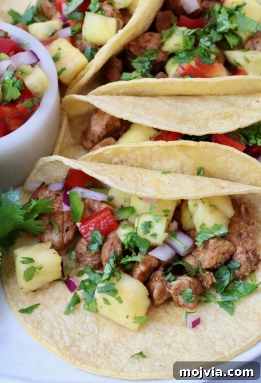 Zesty Carnitas Tacos 7 Two vibrant pork tacos generously topped with pineapple salsa and cilantro, served on a white plate, ready to be enjoyed.