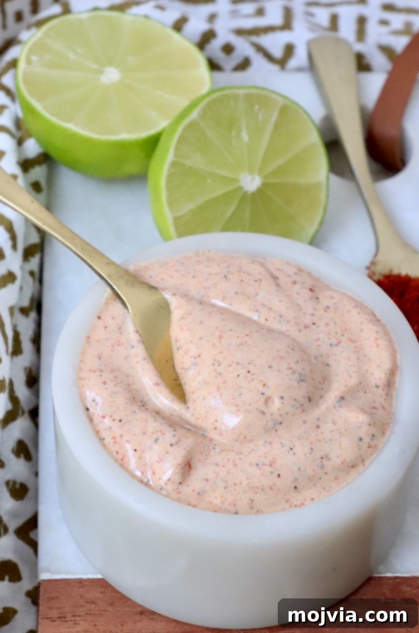 Zesty Chili Lime Vinaigrette 2 A small white bowl filled with creamy chili lime dressing, with a miniature spoon resting inside, ready to be served.