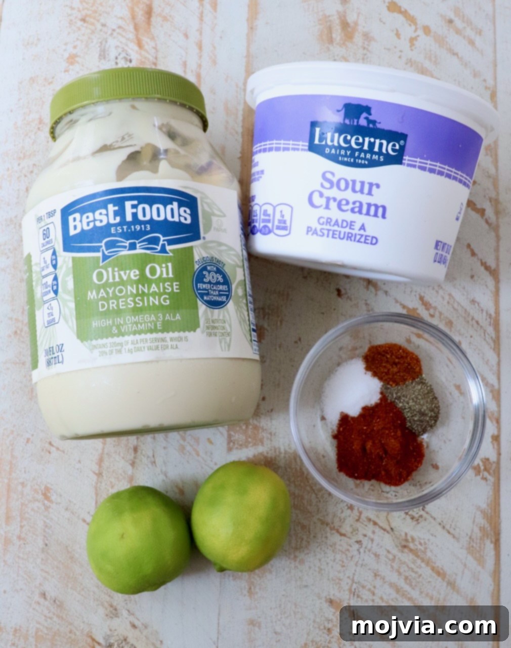 Zesty Chili Lime Vinaigrette 3 Six simple ingredients for chili lime dressing laid out on a white wooden board: sour cream, mayonnaise, limes, chili powder, salt, and cayenne pepper.