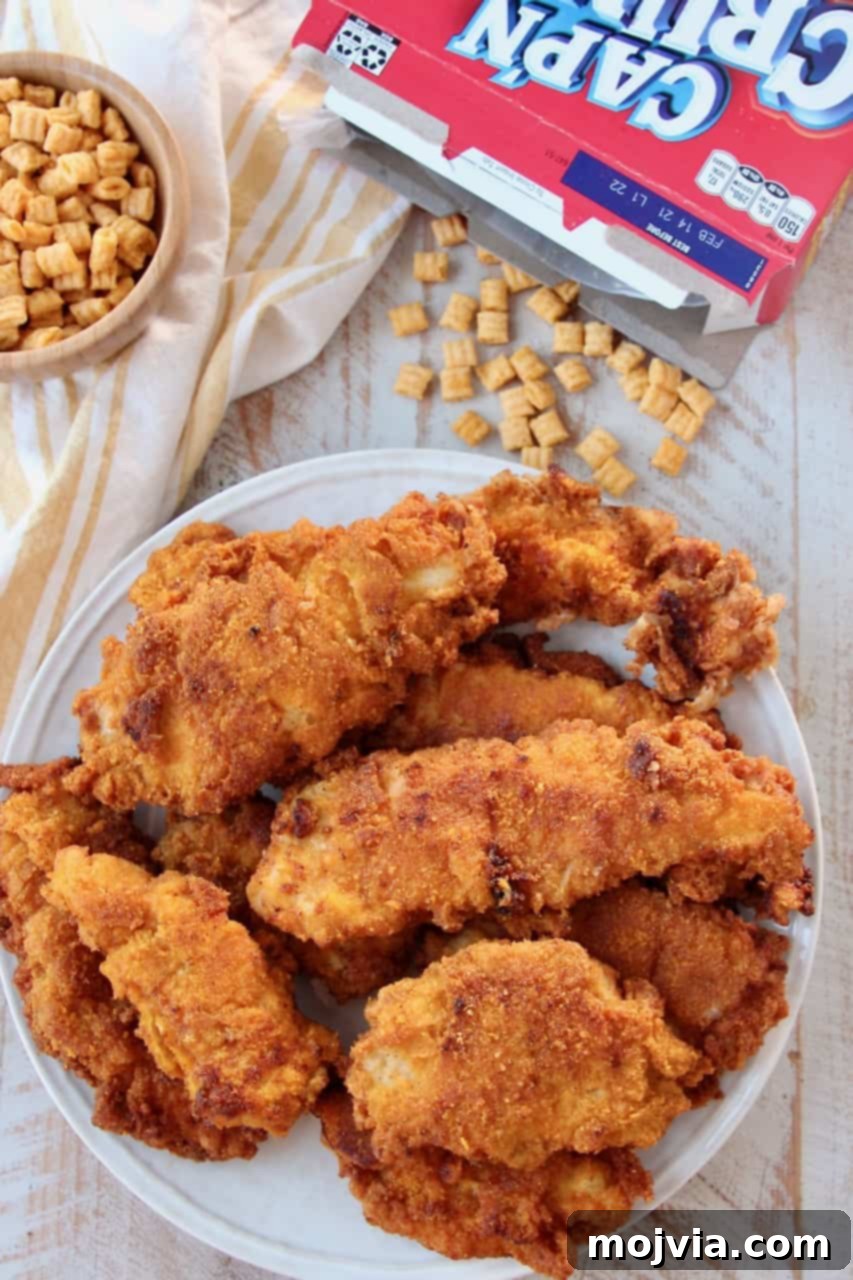 Dads Signature Captain Crunch Chicken Tenders 2 Stacked Captain Crunch fried chicken tenders on a plate with a box of Captain Crunch cereal in the background.