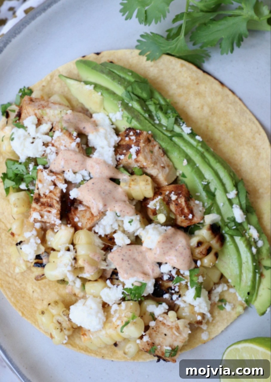Elote Chicken Tacos 2 Grilled chicken street corn tacos beautifully arranged on a plate, garnished with creamy avocado slices and a drizzle of chili lime sauce