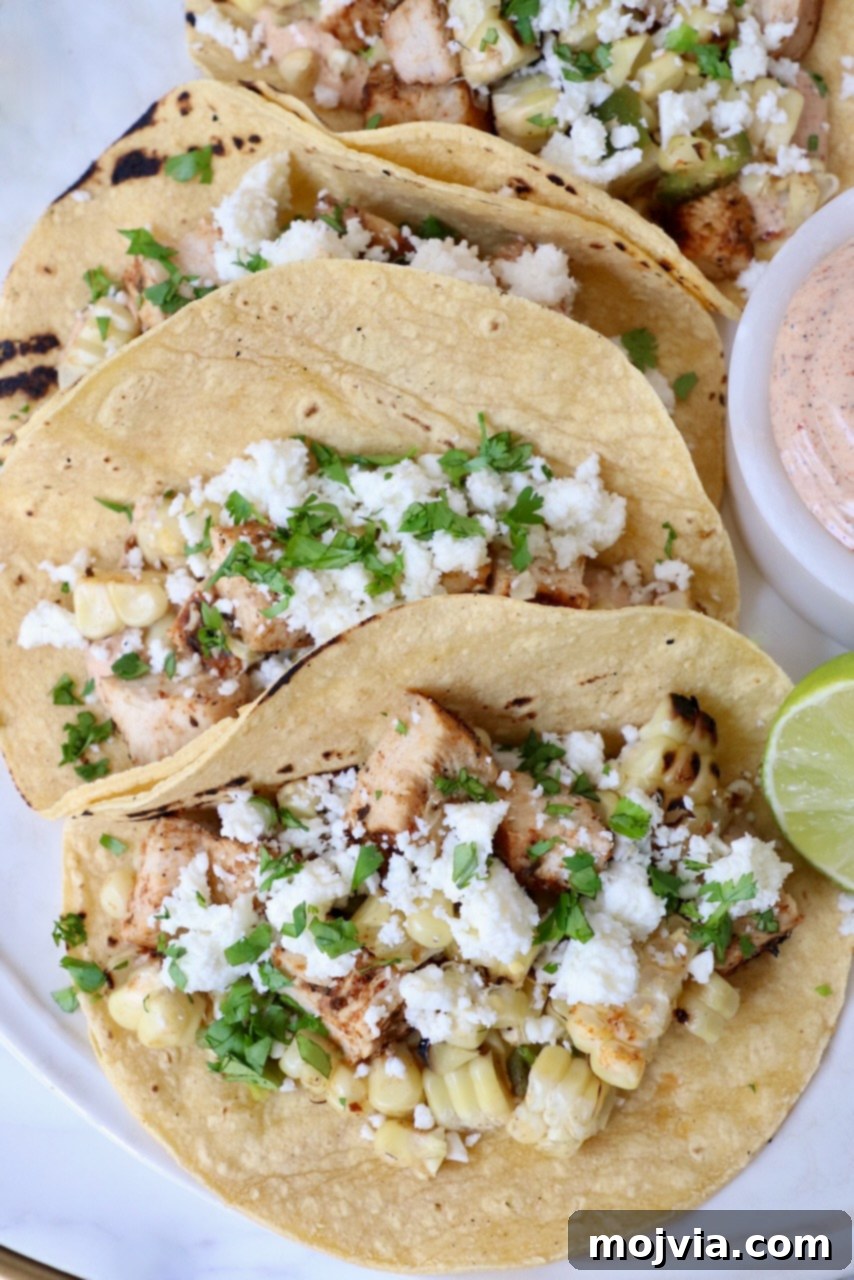 Elote Chicken Tacos 11 Two generously filled street corn and chicken tacos on a plate, garnished with a fresh lime wedge, ready to be served