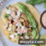 A perfectly assembled street corn and chicken taco on a white plate, topped with diced chicken, corn kernels, and fresh avocado slices, ready to be enjoyed