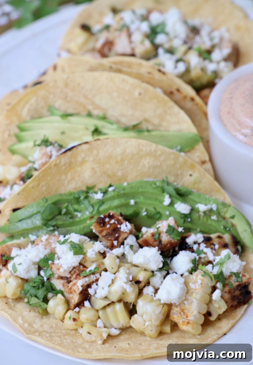 Elote Chicken Tacos 10 A vibrant plate of finished street corn and chicken tacos, filled with diced chicken, grilled corn, and topped with creamy avocado slices, ready to be enjoyed