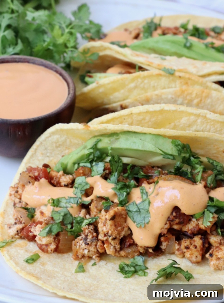 tacos on plate filled with crumbled tofu, chipotle sauce and avocado slices