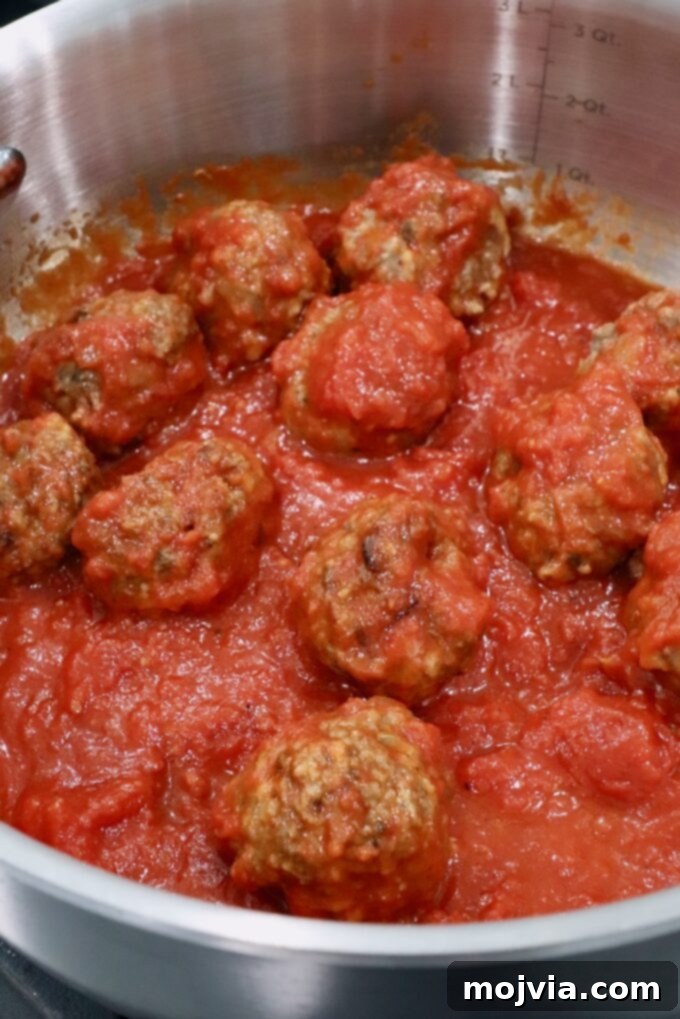 Meatballs simmering in a rich marinara sauce in a large pan on the stovetop.