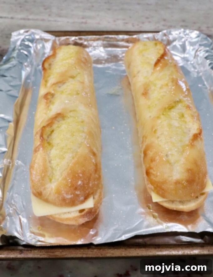 Baguette halves with mozzarella cheese arranged on a foil-lined baking sheet, ready for melting.