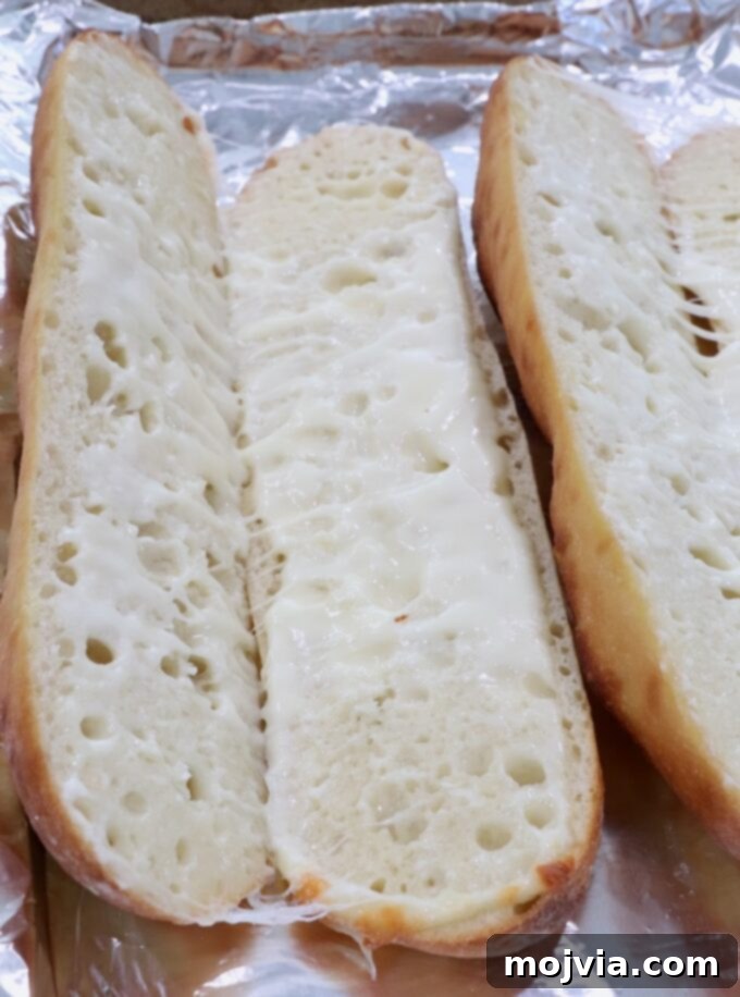 Melted mozzarella cheese beautifully bubbling inside a sliced baguette on a baking sheet.