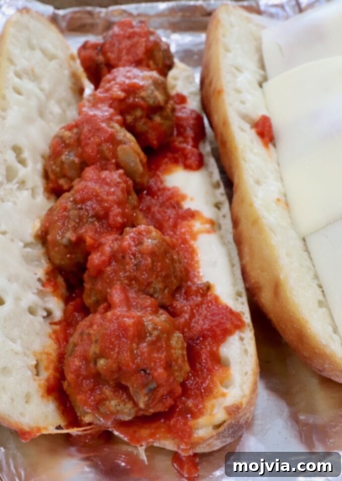 A baguette half generously filled with marinara-coated meatballs and topped with melted mozzarella cheese.