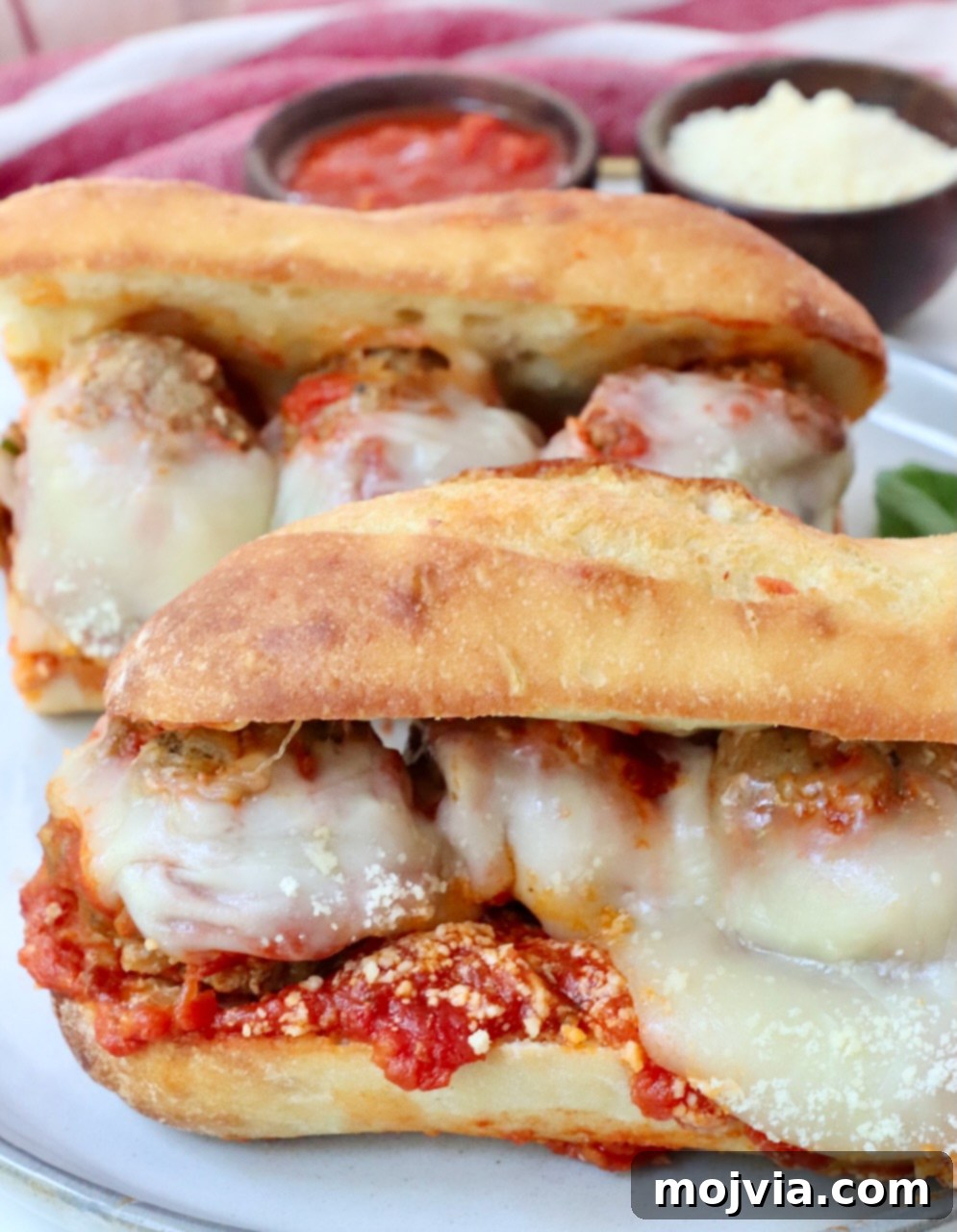 Two perfectly prepared Italian meatball subs, sliced and ready to eat on a serving plate.