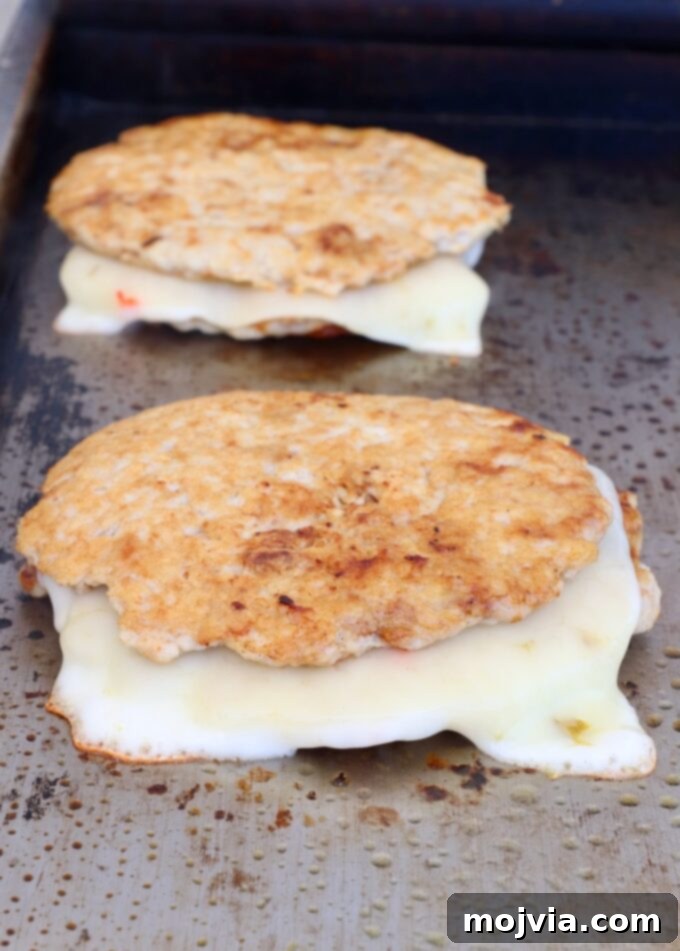 Spicy Buffalo Chicken Smash Burger 9 cooked chicken burger patties stacked up with slices of pepper jack cheese melted in the middle on a griddle
