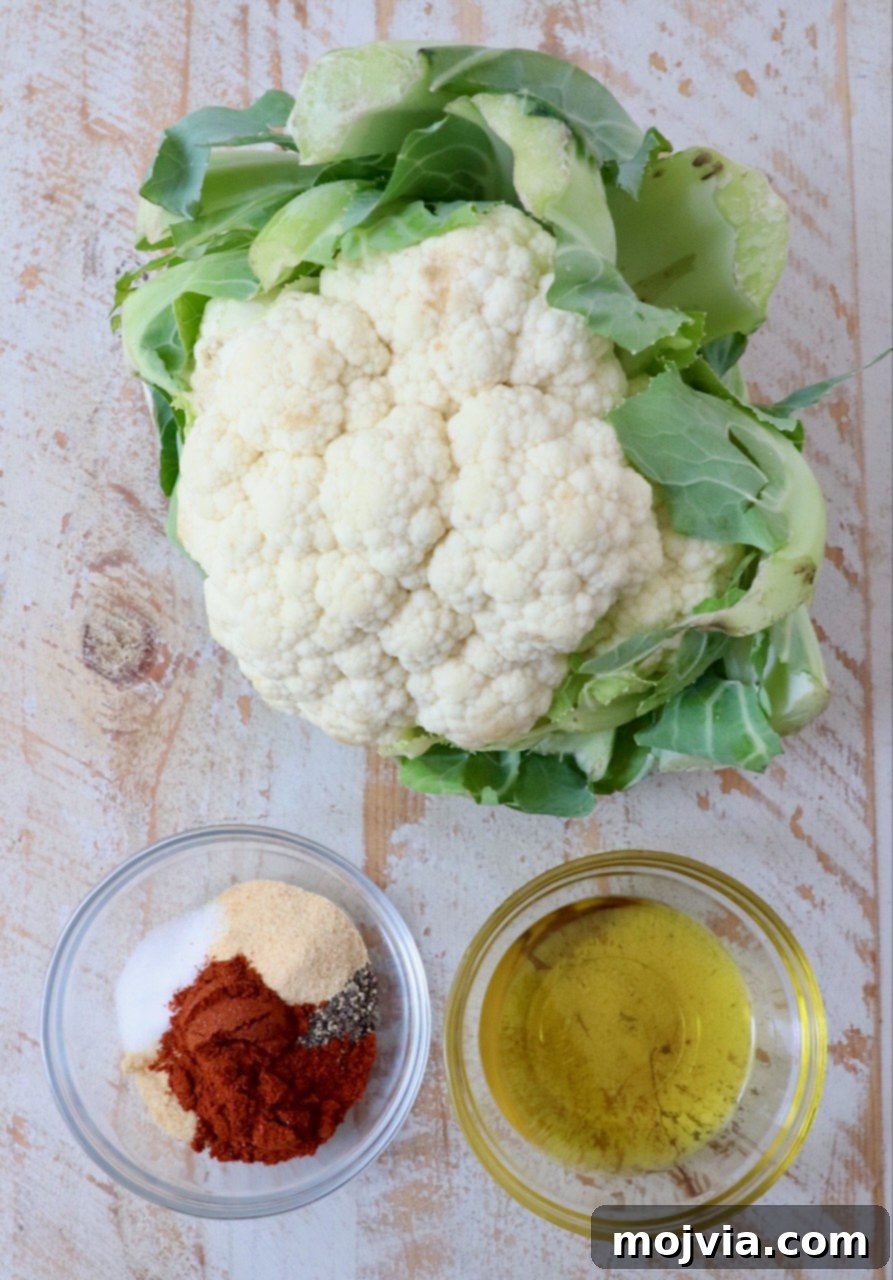 Golden Roasted Cauliflower 3 A fresh head of cauliflower sits beside small bowls of olive oil and a custom spice blend, ready for preparation.