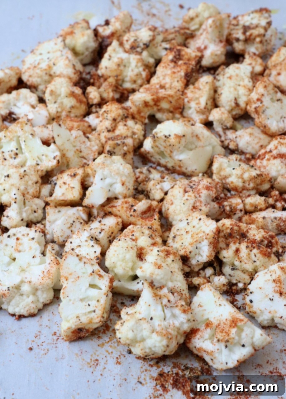 Golden Roasted Cauliflower 4 Cauliflower florets seasoned with herbs and spices, spread in an even layer on a parchment-lined baking sheet, ready for roasting.