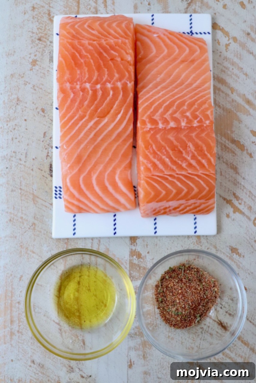 Crispy Air Fryer Salmon 4 Fresh salmon fillets alongside a small bowl of olive oil and a bowl of salmon seasoning, ready for preparation.