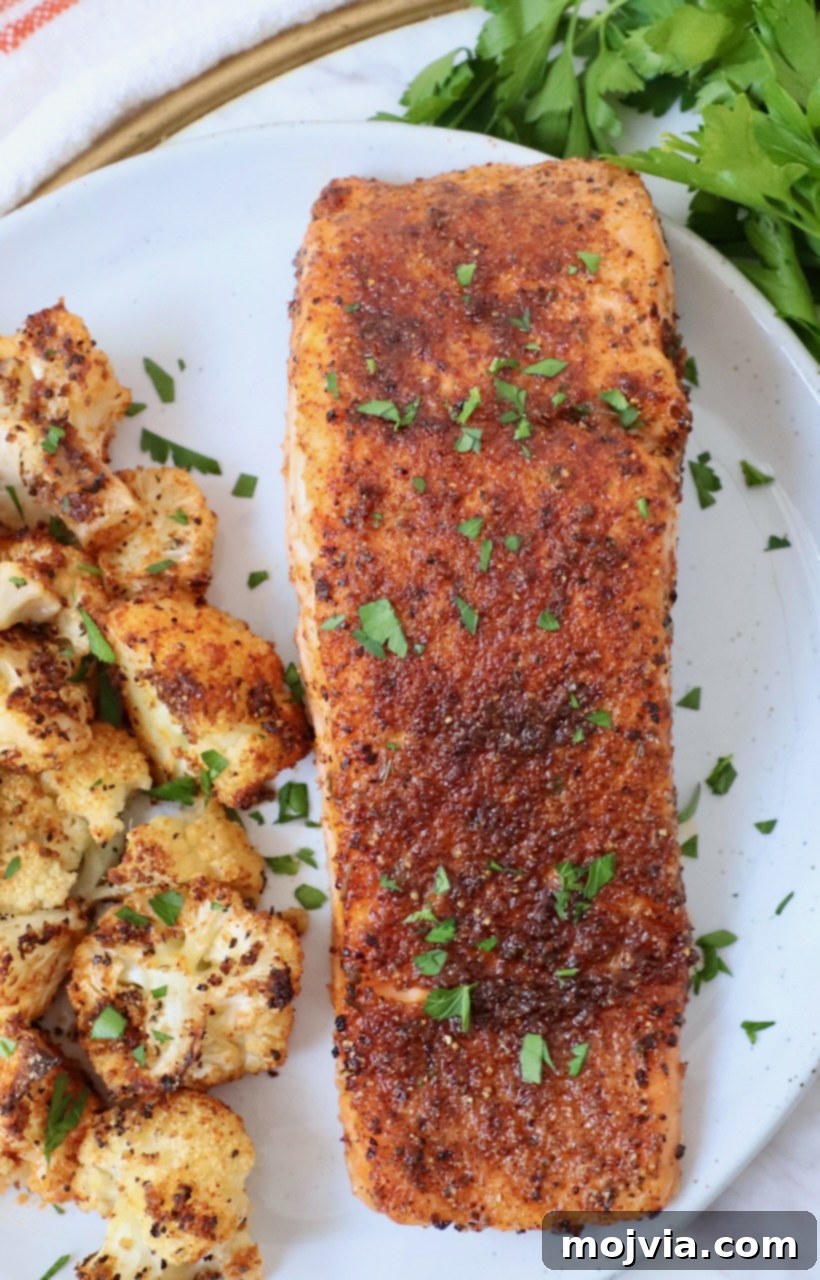 Crispy Air Fryer Salmon 7 Close-up of a perfectly cooked and seasoned air fryer salmon fillet on a plate with roasted cauliflower in the background.