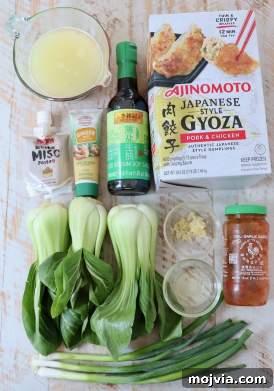 Comforting Gyoza Dumpling Soup 3 All the fresh ingredients for Gyoza Soup laid out on a white wooden board, including frozen gyoza, green onions, garlic, ginger paste, bok choy, and various sauces.