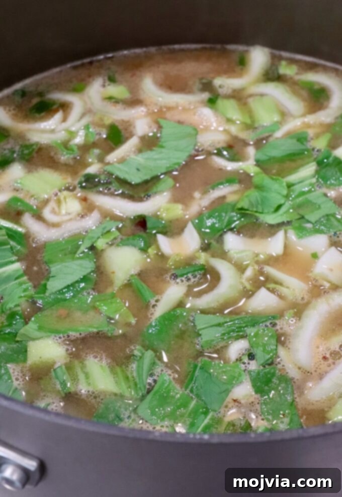 Comforting Gyoza Dumpling Soup 6 Chopped baby bok choy added to a simmering pot of broth on the stove, beginning to tenderize.