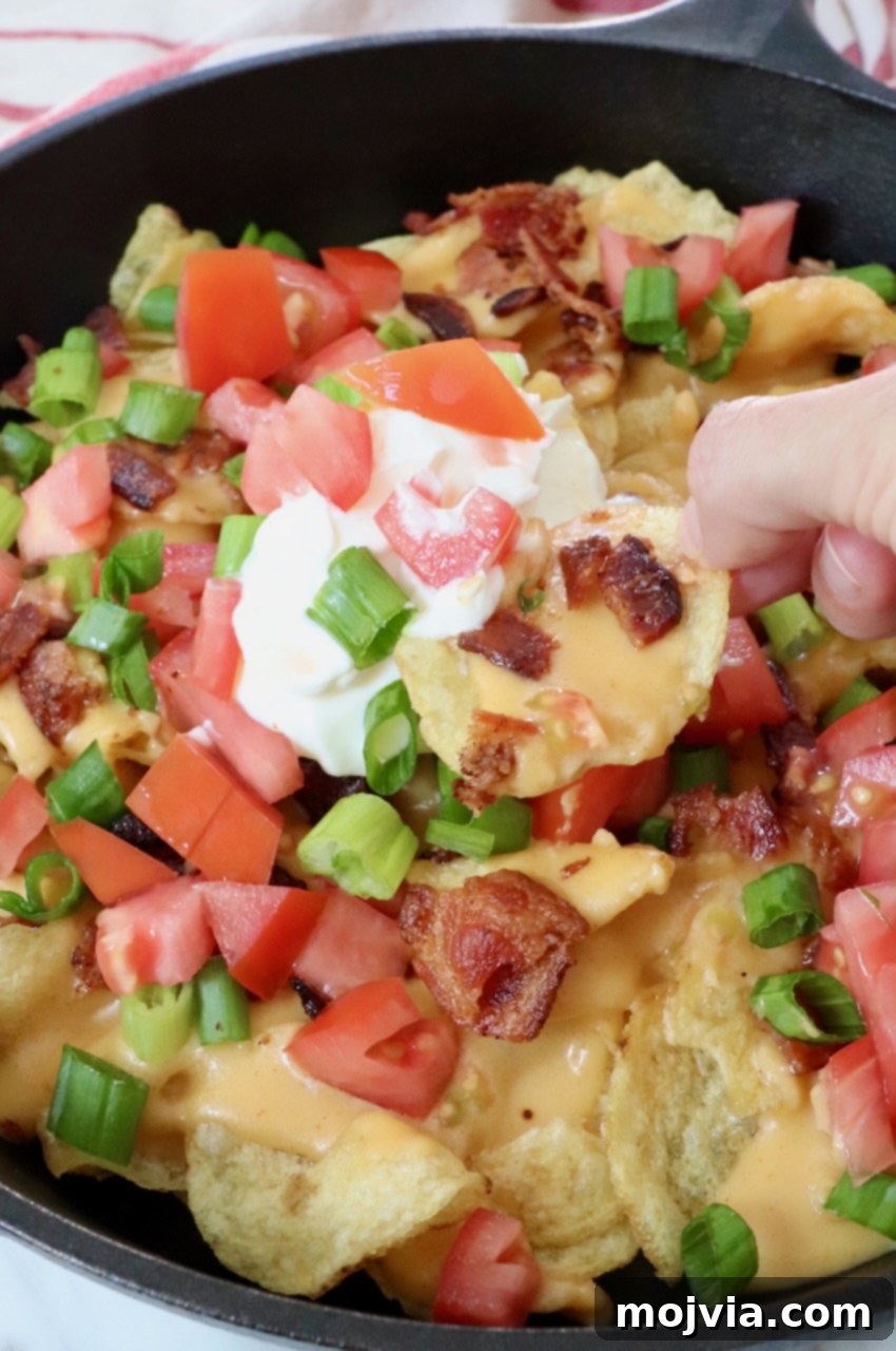 Emerald Potato Nachos 2 A cast iron skillet brimming with golden Irish nachos, topped with a generous dollop of sour cream, ready to be devoured.