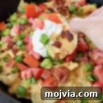 Hand dipping a chip into sour cream in a skillet of Irish nachos, ready to eat.