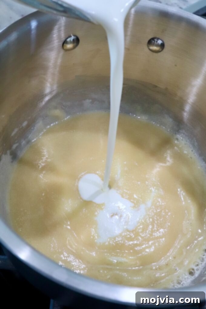Emerald Potato Nachos 4 Heavy cream being slowly poured into a roux in a saucepan on the stove, beginning the beer cheese sauce process.