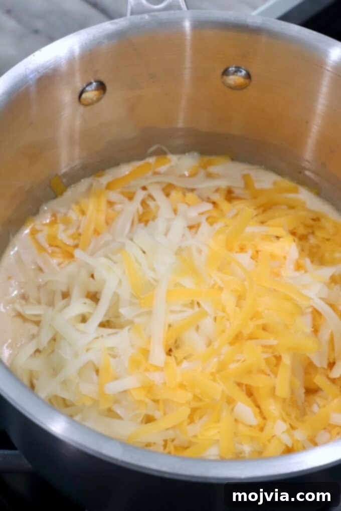Emerald Potato Nachos 5 Shredded cheddar and Swiss cheese being added to a simmering creamy sauce in a pot on the stove, stirring to melt.