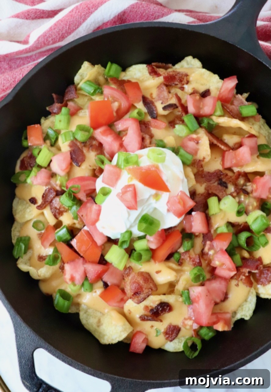 Emerald Potato Nachos 6 A close-up shot of Irish nachos generously topped with melted cheese sauce, a central dollop of sour cream, and fresh garnishes in a skillet.
