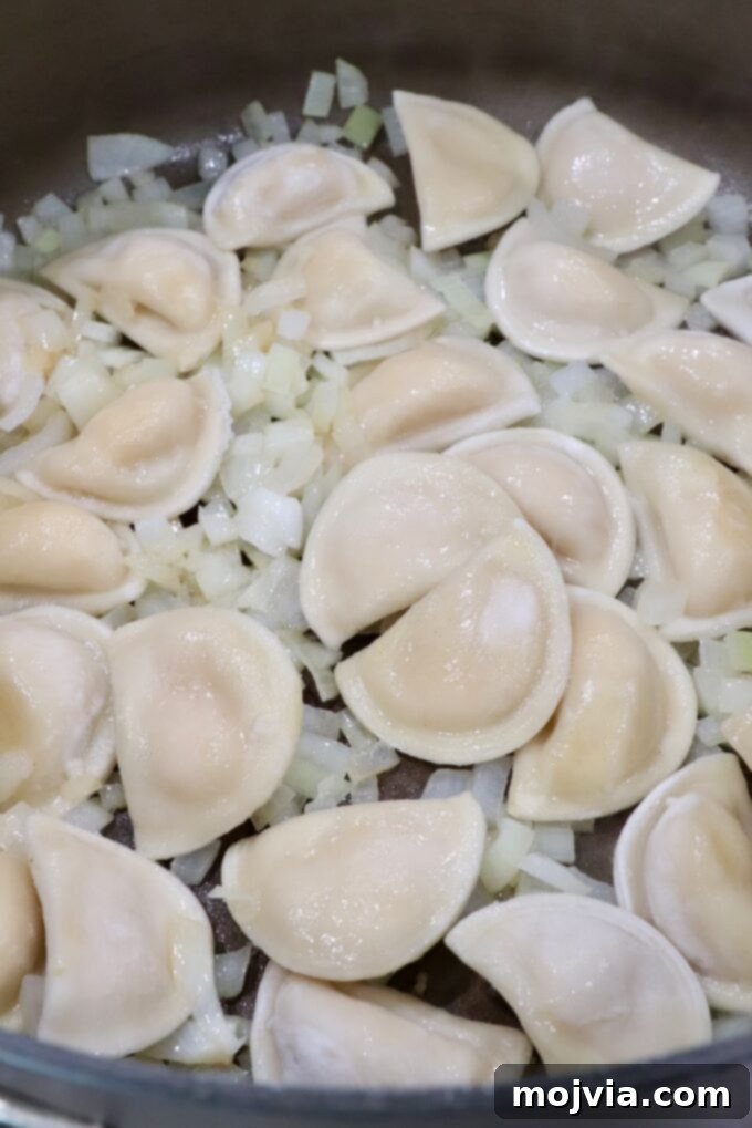 Hearty Pierogi Soup 4 Frozen mini pierogis and diced onions cooking in a large pot with melted butter.