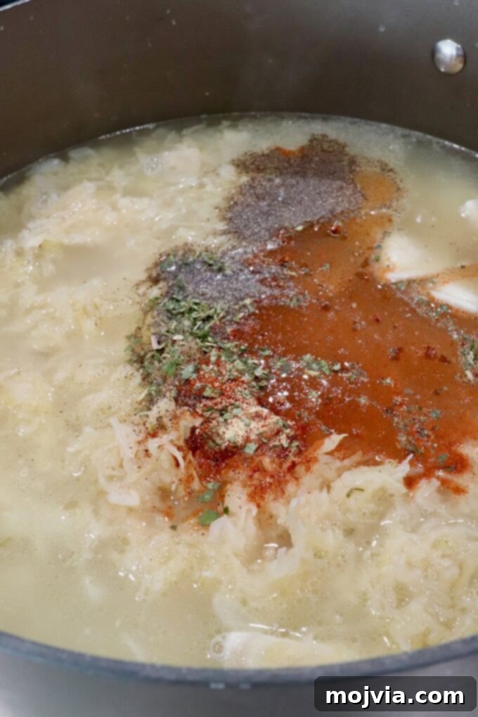 Hearty Pierogi Soup 6 Seasonings being sprinkled into a pot of chicken broth, sauerkraut, onions, and pierogis, ready to simmer.