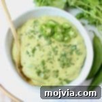 Creamy green salsa in bowl with gold spoon and serrano peppers