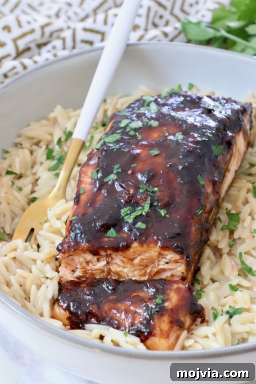 Sticky Balsamic Glazed Salmon 2 Cooked balsamic glazed salmon on a bed of orzo in a bowl with a fork, garnished with fresh herbs.
