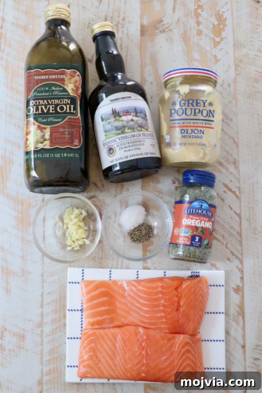 Sticky Balsamic Glazed Salmon 3 Ingredients for balsamic glazed salmon laid out on a white wooden board, including fresh garlic, balsamic vinegar, Dijon mustard, and salmon fillets.