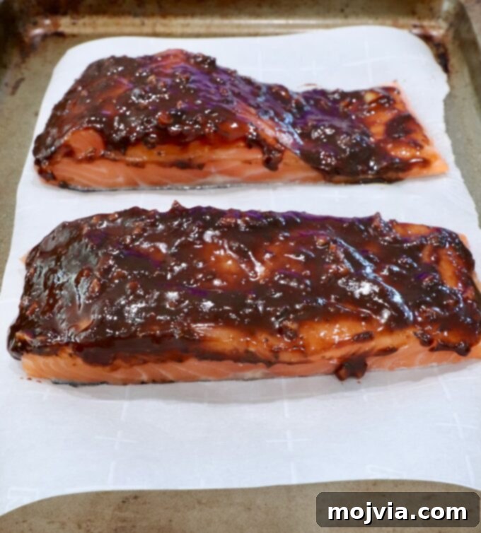 Sticky Balsamic Glazed Salmon 5 Balsamic glazed salmon fillets arranged on a piece of parchment paper on a baking sheet, ready for the oven.